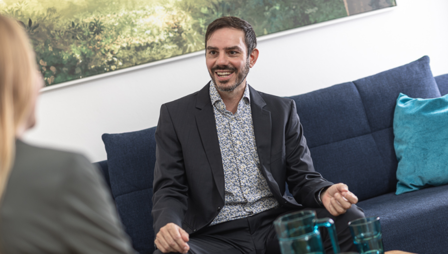 Coach Christian Ploy im Anzug auf einer Couch sitzend beim Interview